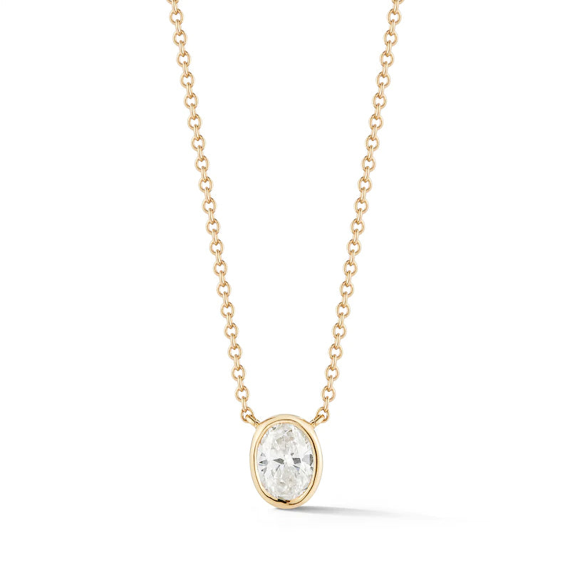 The Bezel Set Oval Diamond Solitaire Pendant in Yellow Gold features an oval diamond in a sleek 18k yellow gold bezel setting. The image shows the pendant against a white background.
