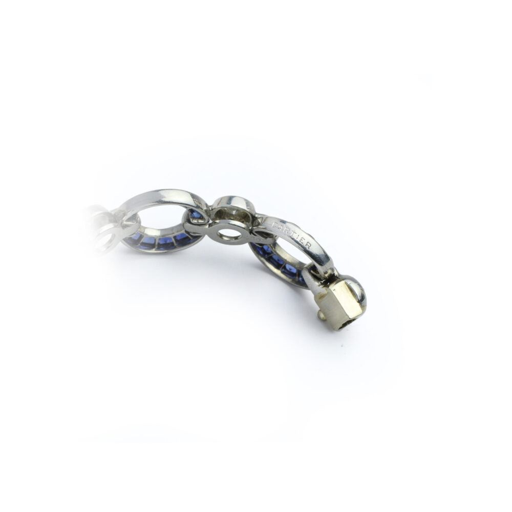 Close-up of a Cartier Art Deco Sapphire and Diamond Watch featuring silver oval links, some with sapphire-blue stones, and a gold clasp, displayed on a white background.
