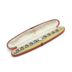A Cartier Art Deco Sapphire and Diamond Watch is displayed in an open, red, oval jewelry case lined with cream-colored fabric.