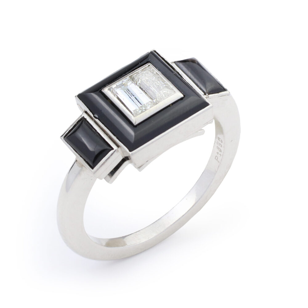 The Onyx and Diamond Ring showcases a platinum band with a rectangular setting, a central clear gemstone, framed by onyx and accented with black rectangles and small black squares at each end.