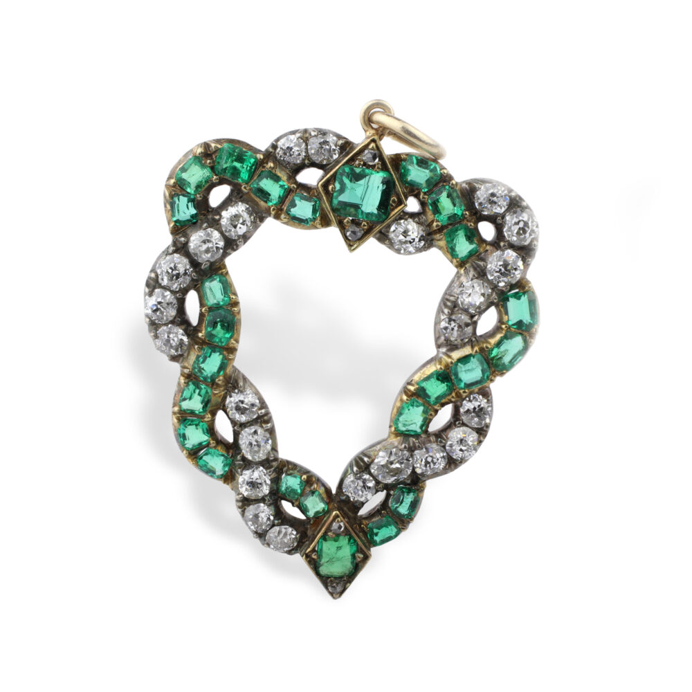 The Emerald and Diamond Heart Pendant features a twisted open-heart design in gold, with alternating cushion-shaped emeralds and old-cut diamonds, and a small loop at the top for hanging.