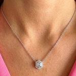A close-up of a woman’s neck wearing the Pavé Hexagonal Diamond Solitaire Pendant in White Gold, featuring a geometric hexagon design. She pairs the necklace with a pink top.