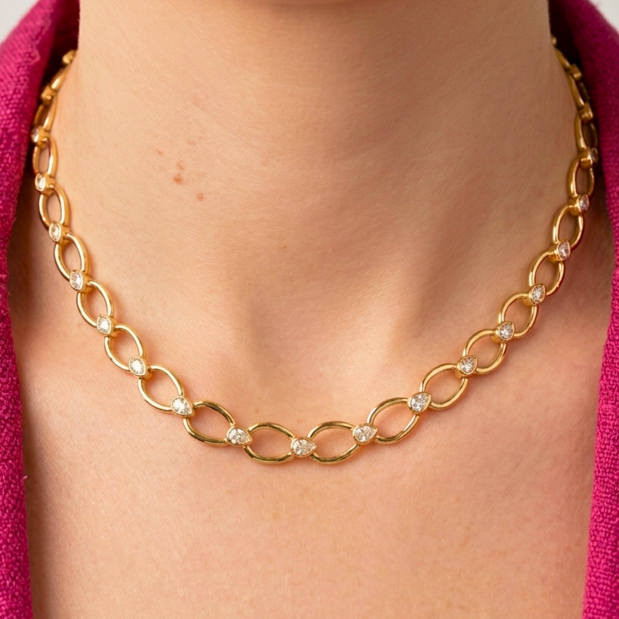 A close-up of a person wearing the Pear Shape Link Necklace with Bezel Set Pear Shape Diamonds in yellow gold, paired with a pink textured garment.