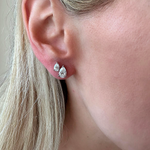 Close-up of a light-skinned, blonde-haired person wearing the Duo Studs in White Gold with Pear Diamonds: one small round and one larger pear-shaped diamond stud, both set in 18K white gold.
