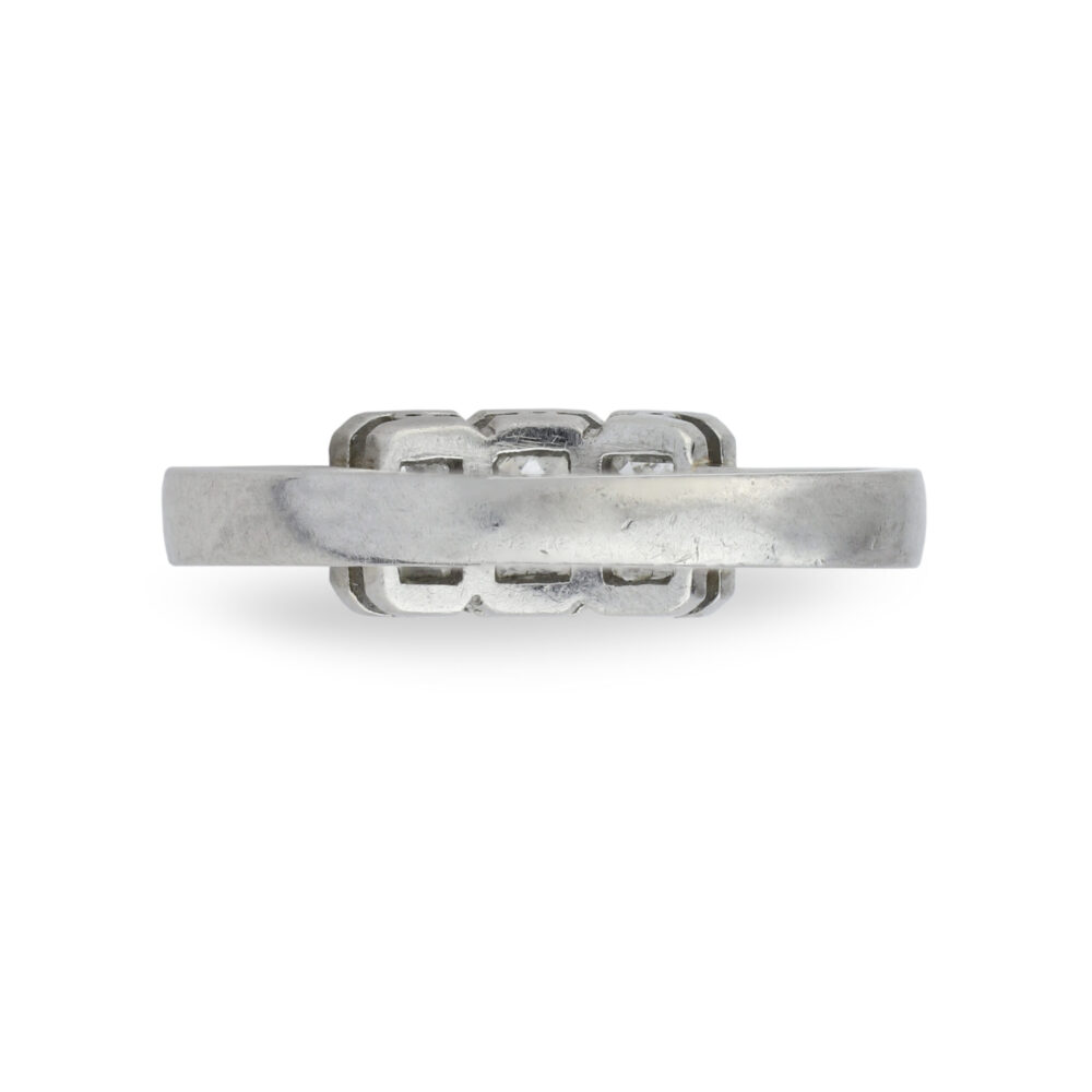 A Three-Stone Diamond Ring with a flat, wide silver band and a geometric, vintage-inspired design at the top is shown from the side against a white background.