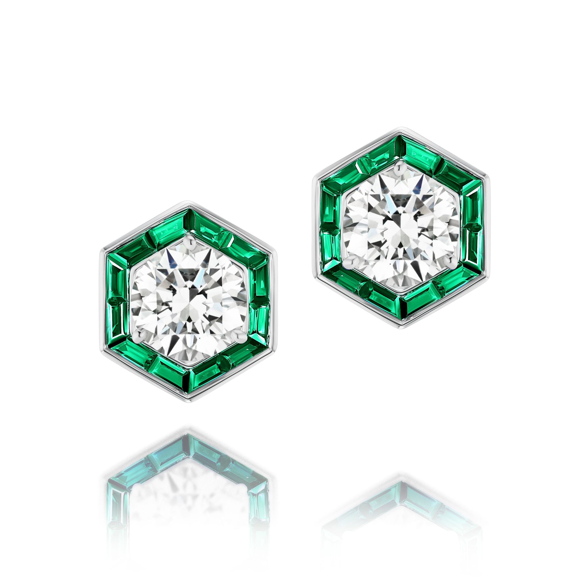 Hexagonal Trapezoid Emerald Stud Ear Jackets in White Gold, each featuring a prominent central round diamond encircled by vibrant trapezoid baguette emeralds and set in 18k white gold, elegantly displayed on a white reflective surface.