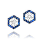 Hexagonal Trapezoid Sapphire Stud Ear Jackets featuring silver construction with blue gemstone borders and a striking sunburst center are elegantly displayed on a white reflective surface.