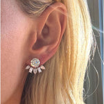 A close-up of a woman's ear showcases the Alternating Pear Shape and Emerald Cut Diamond Ear Jackets, featuring a dazzling emerald-cut diamond accented by five smaller, baguette-inspired stones arranged in an elegant fan shape reminiscent of modern ear jackets. Partially visible blonde hair and sunlight draw attention to the shimmering jewelry.