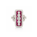 The Vintage Ruby and Diamond Ring showcases a rectangular design accented with a row of five old European-cut diamonds at its center. Vivid calibré-cut rubies border the diamonds, while smaller diamonds further enhance the piece. This ring is set in platinum and 18K white gold and features intricate decorative side details.