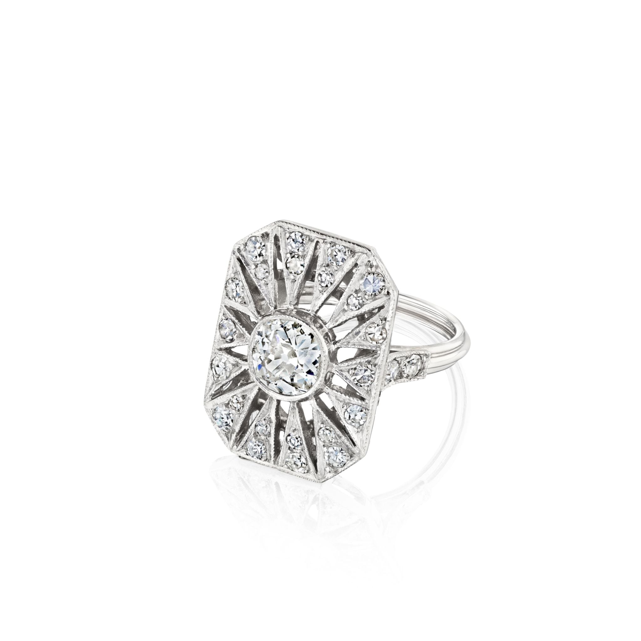 The Art Deco Diamond Ring, crafted in platinum circa 1925, showcases a prominent round old European-cut diamond at its center. Encircled by a geometric sunburst motif embellished with smaller diamonds, the ring is set on a simple band and presented against a white background.
