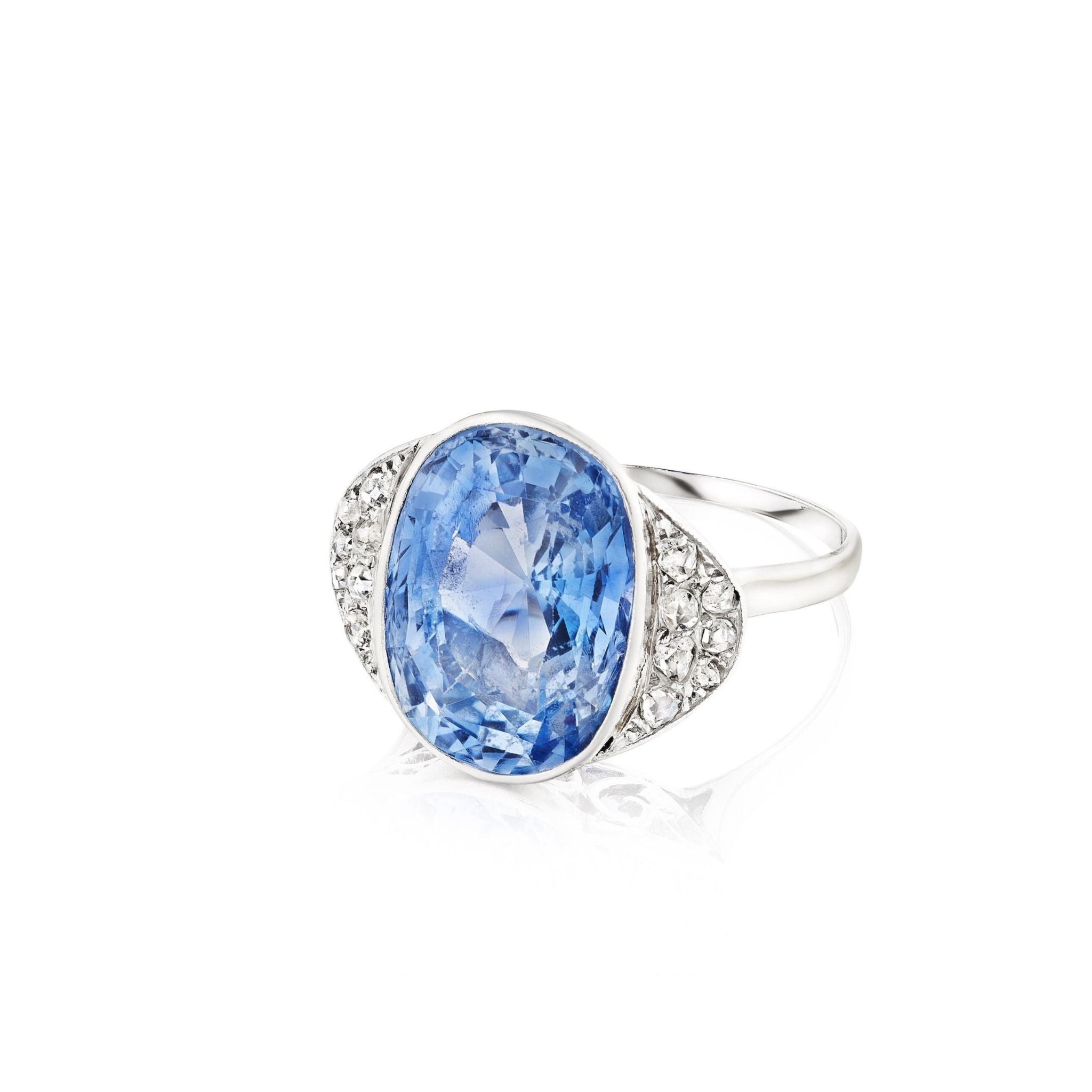1930s Sapphire and Diamond Ring displayed on a white background, featuring a large oval Ceylon sapphire at the center, flanked by clusters of small rose-cut diamonds on each side.