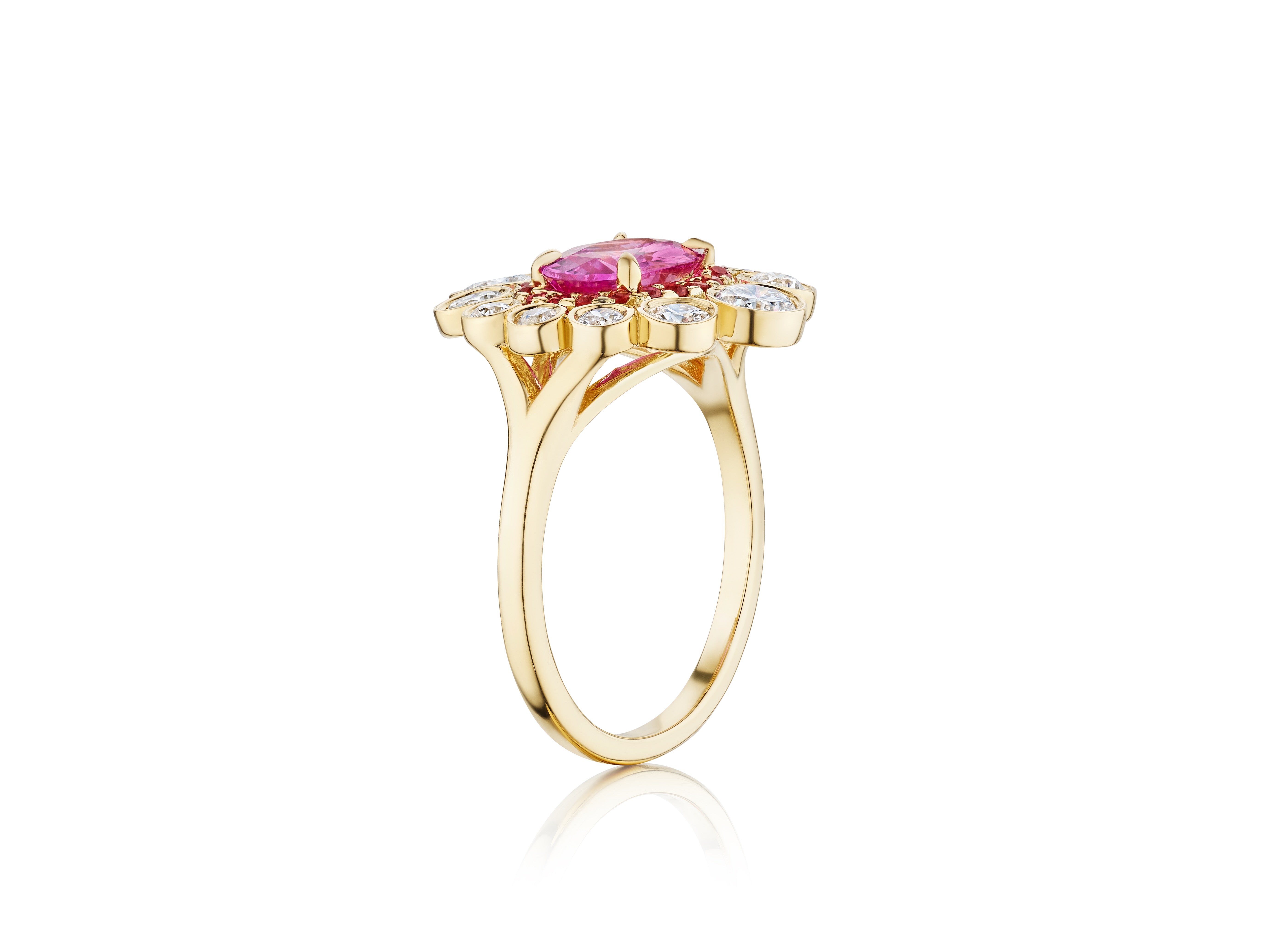 The Cocktail Ring in Yellow Gold features an east-west set oval pink sapphire center, surrounded by a halo of round diamonds, all set in 18K yellow gold and displayed from a side angle on a white background.