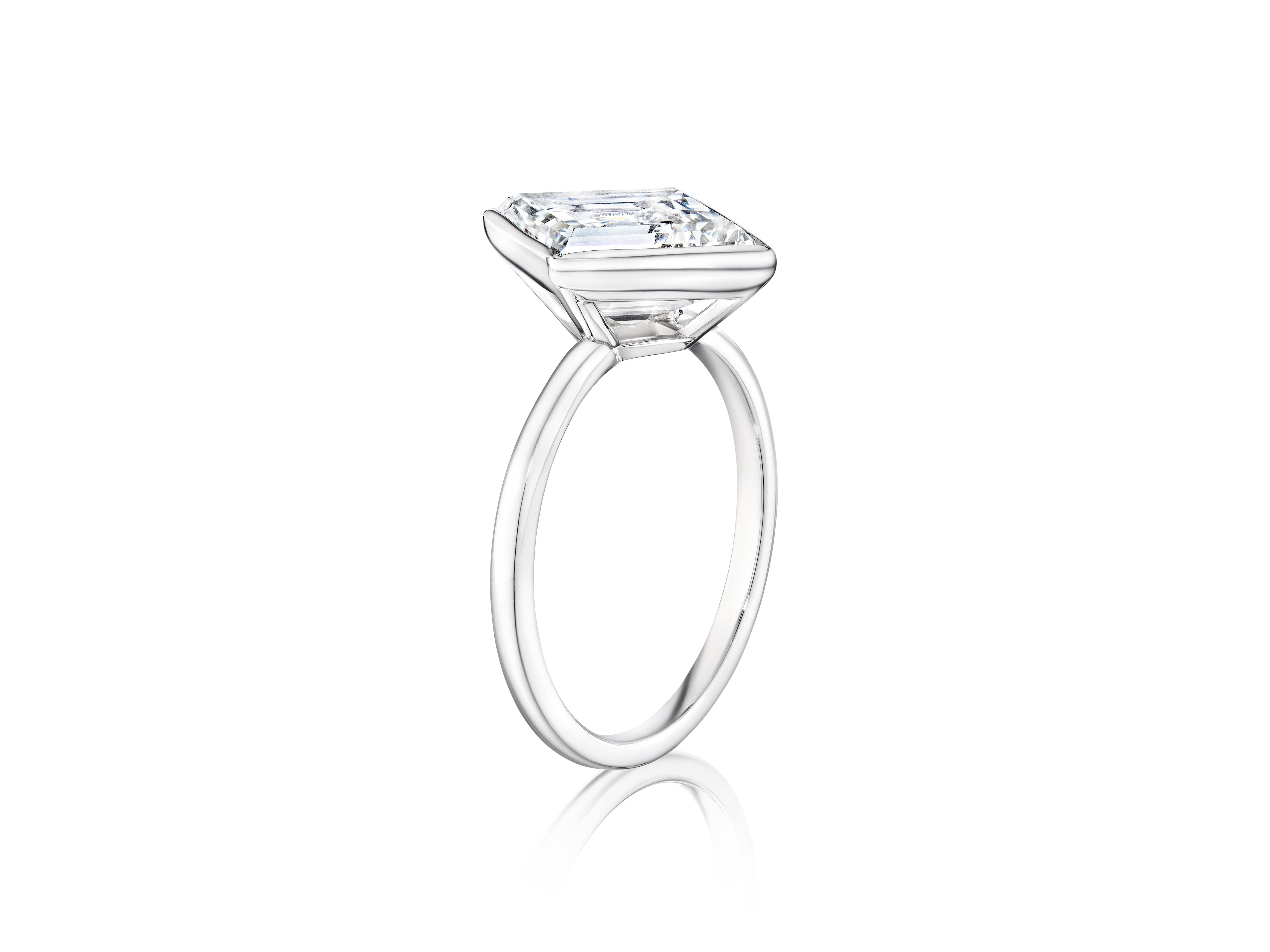 The Bezel Set Lozenge Diamond Engagement Ring showcases a large lozenge-shaped diamond in a sleek bezel setting atop a thin 18K white gold band, displayed against a plain white background.