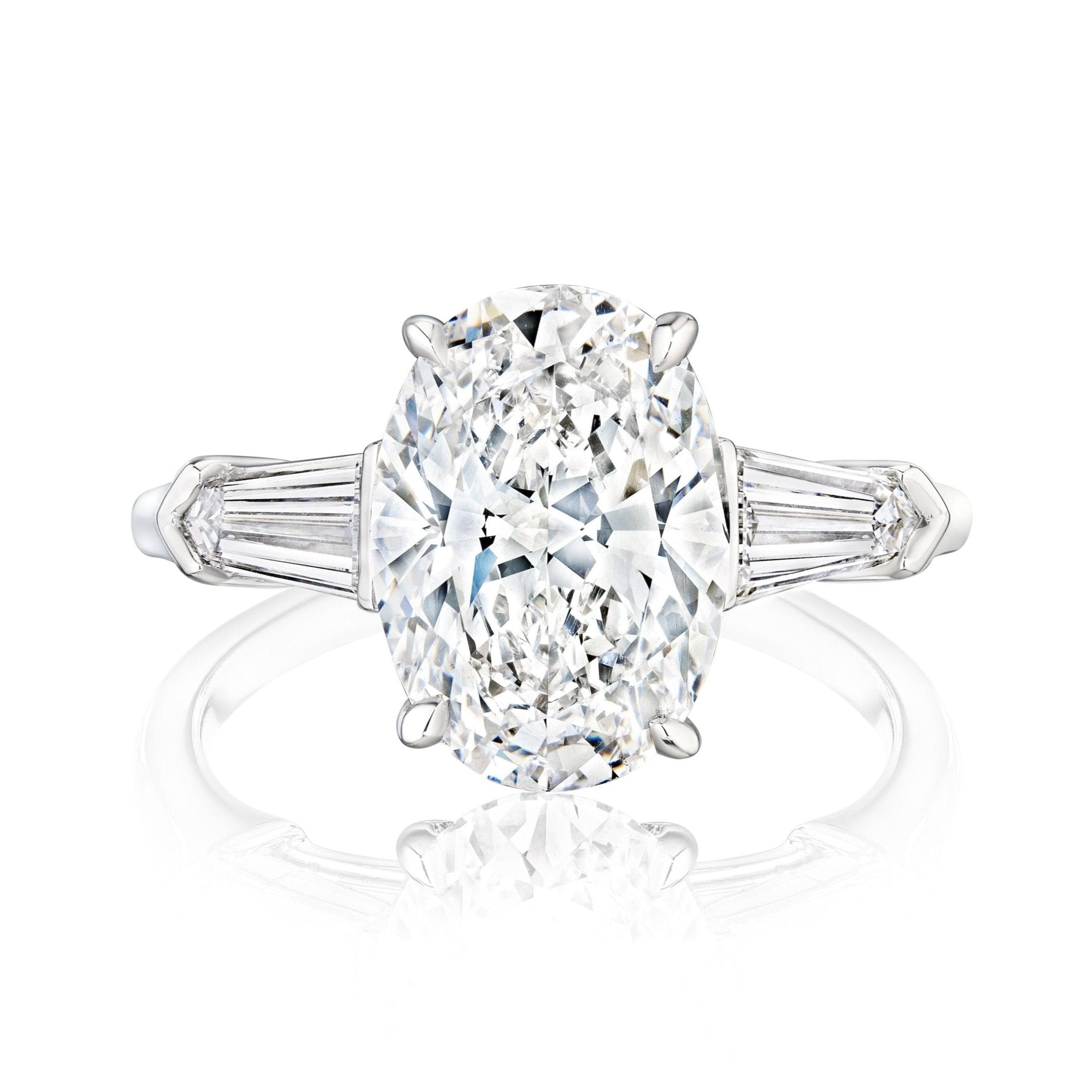 The Oval Shape Diamond Engagement Ring with Tapered Baguette Side Stones showcases a central oval diamond accented by two baguette-cut diamonds on each side, set in white gold and displayed on a white background.