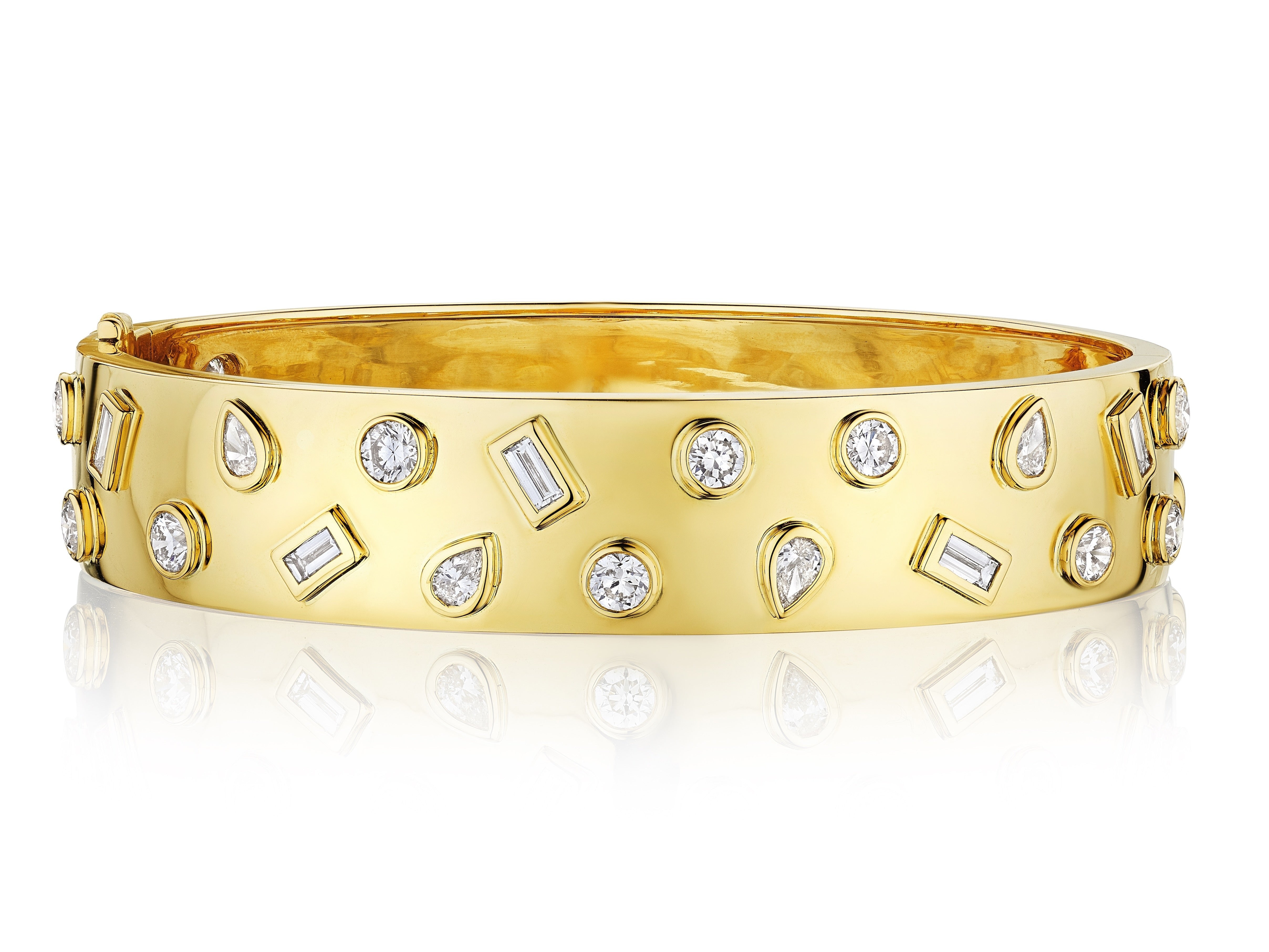 The Bezel Set Mixed Shape Diamond Bangle in Yellow Gold displays round and baguette diamonds with teardrop clear gemstones in a scattered pattern, shown on a reflective white surface.
