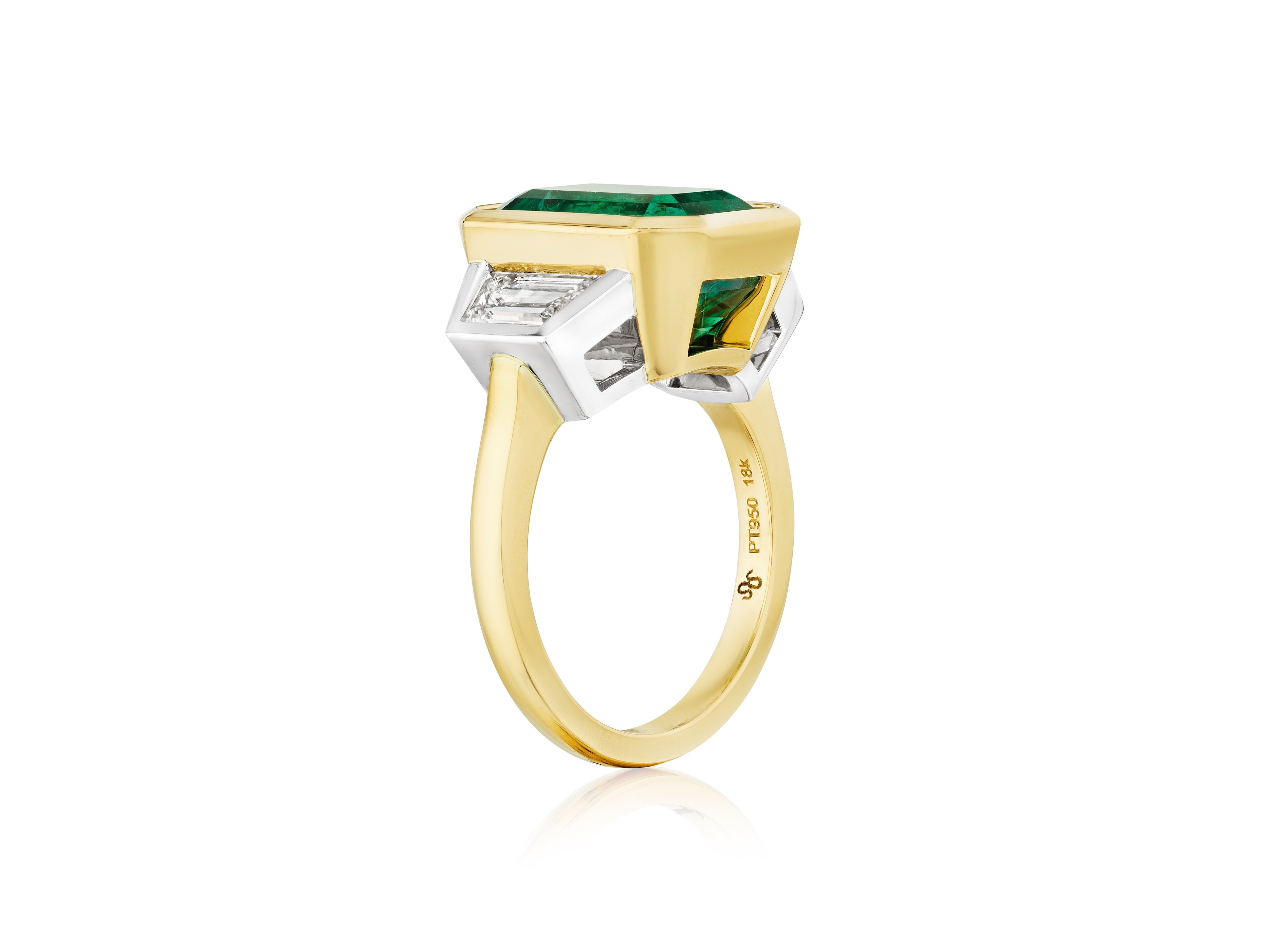 The Bezel Set Emerald Cut Emerald Engagement Ring in Yellow Gold and Platinum features a central emerald, accented by trapezoid baguette diamonds, and is displayed against a white background.