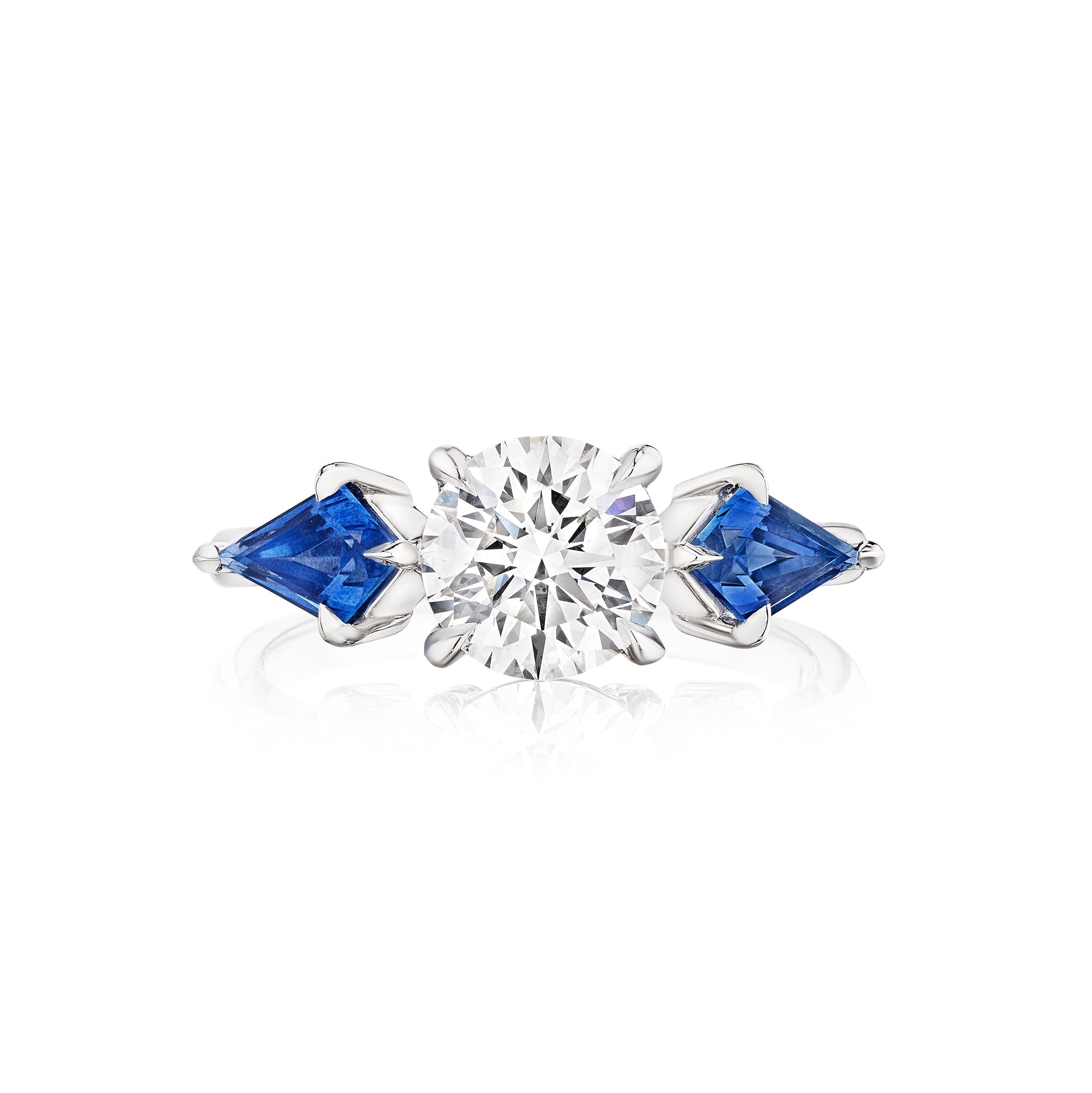 The Bespoke Round Diamond Engagement Ring in White Gold features a central round diamond and kite-shaped blue sapphire side stones.
