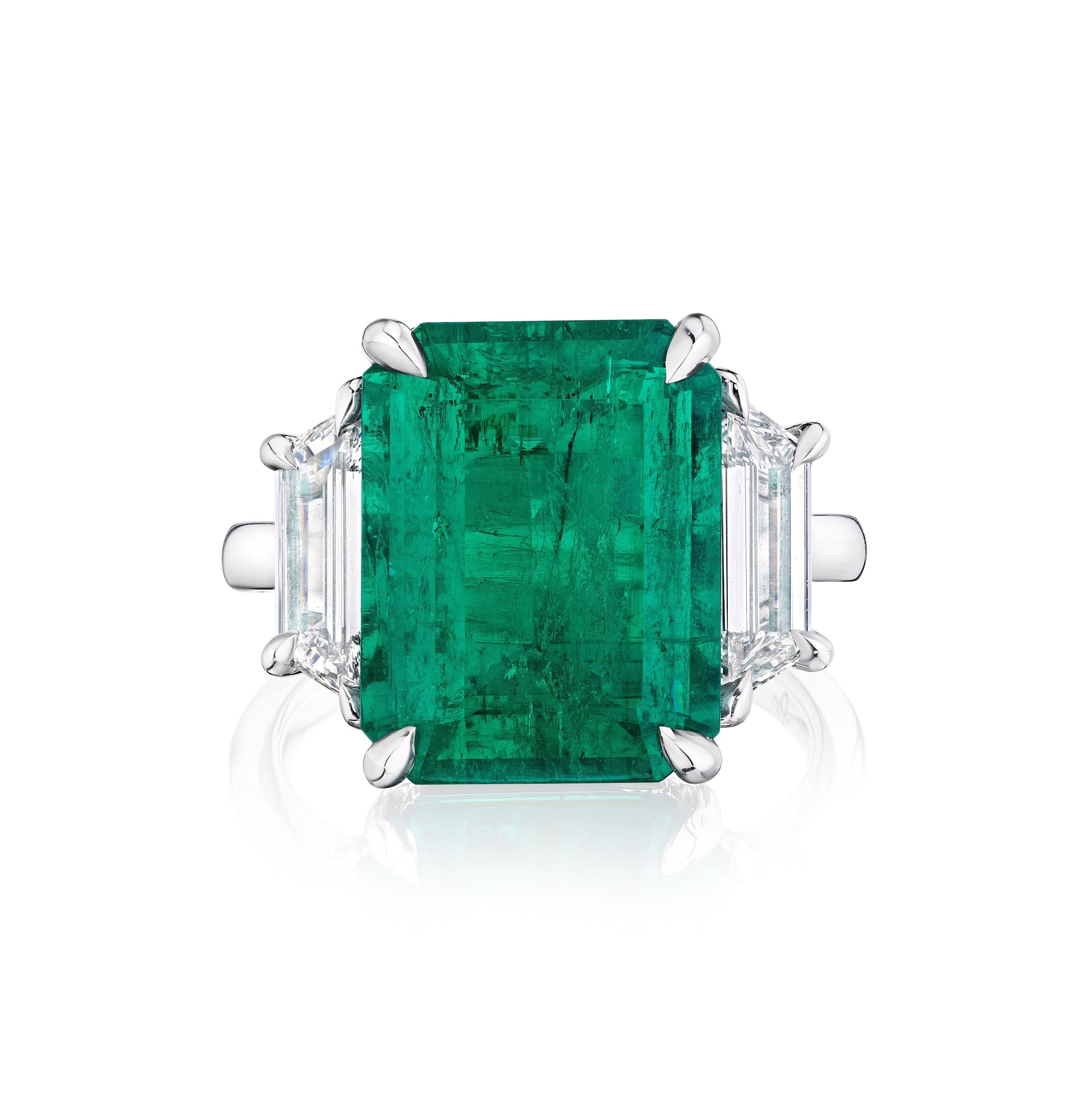 A Bespoke Emerald Cut Colombian Emerald Engagement Ring in white gold features a large emerald and trapezoid baguette side stones, displayed against a white background.