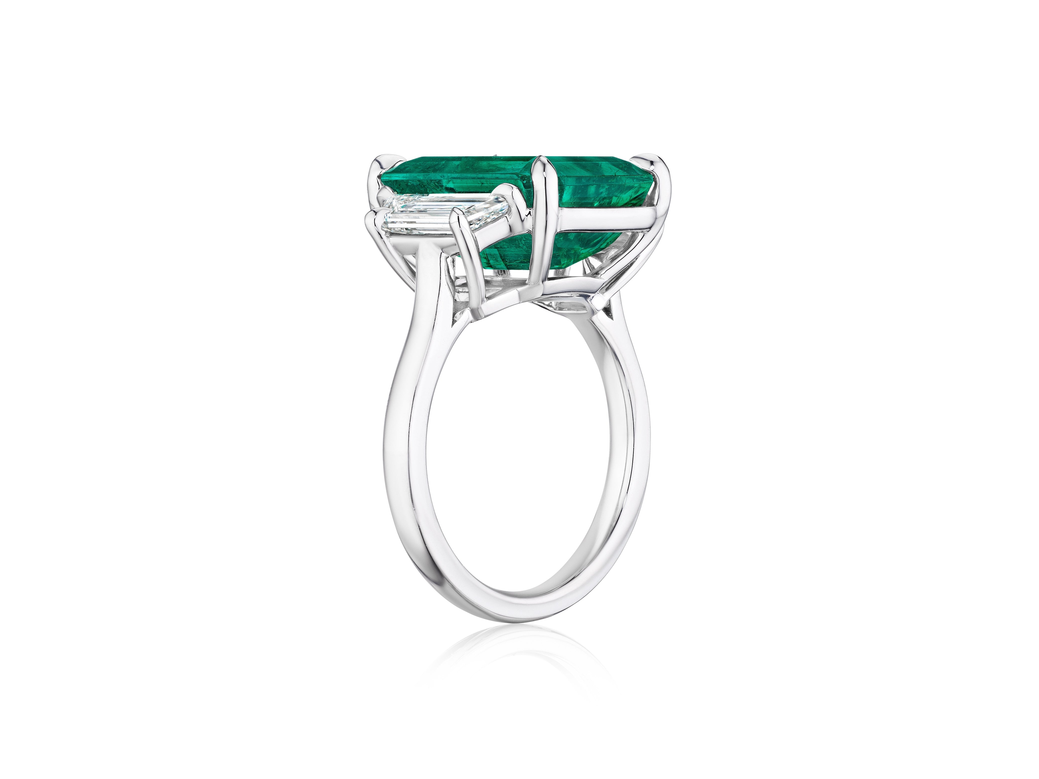 The Bespoke Emerald Cut Colombian Emerald Engagement Ring in white gold features a striking emerald center and trapezoid baguette side stones, showcased against a white background.