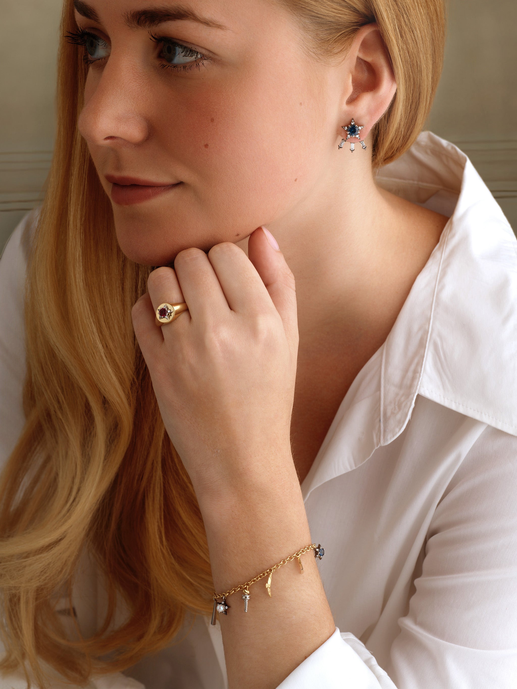 A woman with long blonde hair in a white blouse showcases handcrafted America250 Baguette Diamond Ear Jackets in Black Rhodium, made in New York City. She rests her chin on her hand and gazes to the side.