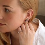 A woman with long blonde hair, in a white shirt and silver floral earrings, rests her hand near her ear wearing the America250 Star and Baguette Sapphire and Diamond Ring in Platinum, along with a delicate star-shaped necklace.