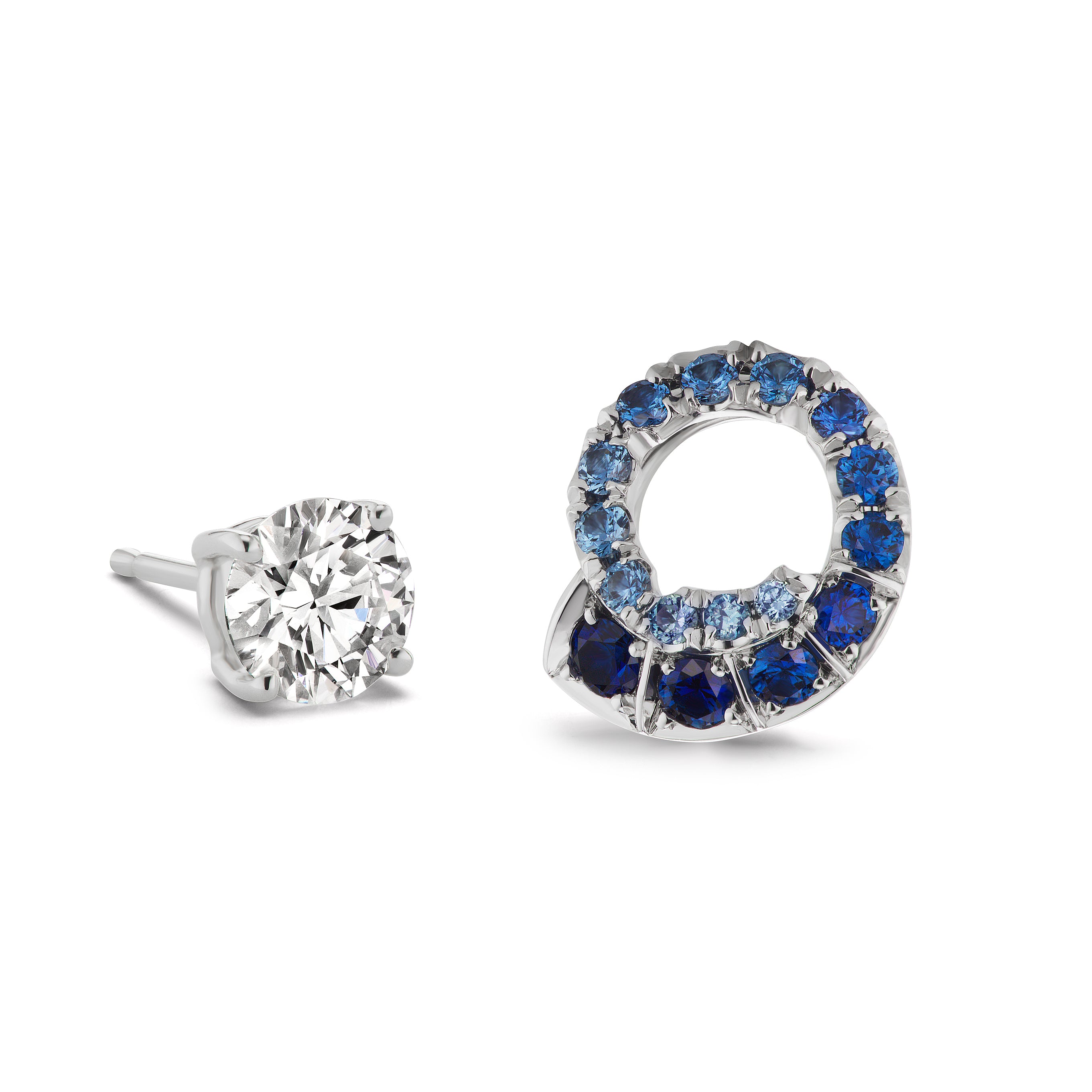 The Ombré Swirl Ear Jackets in white gold feature mismatched earrings: a simple round stud and a spiral design with multicolor sapphires in varying blue tones.