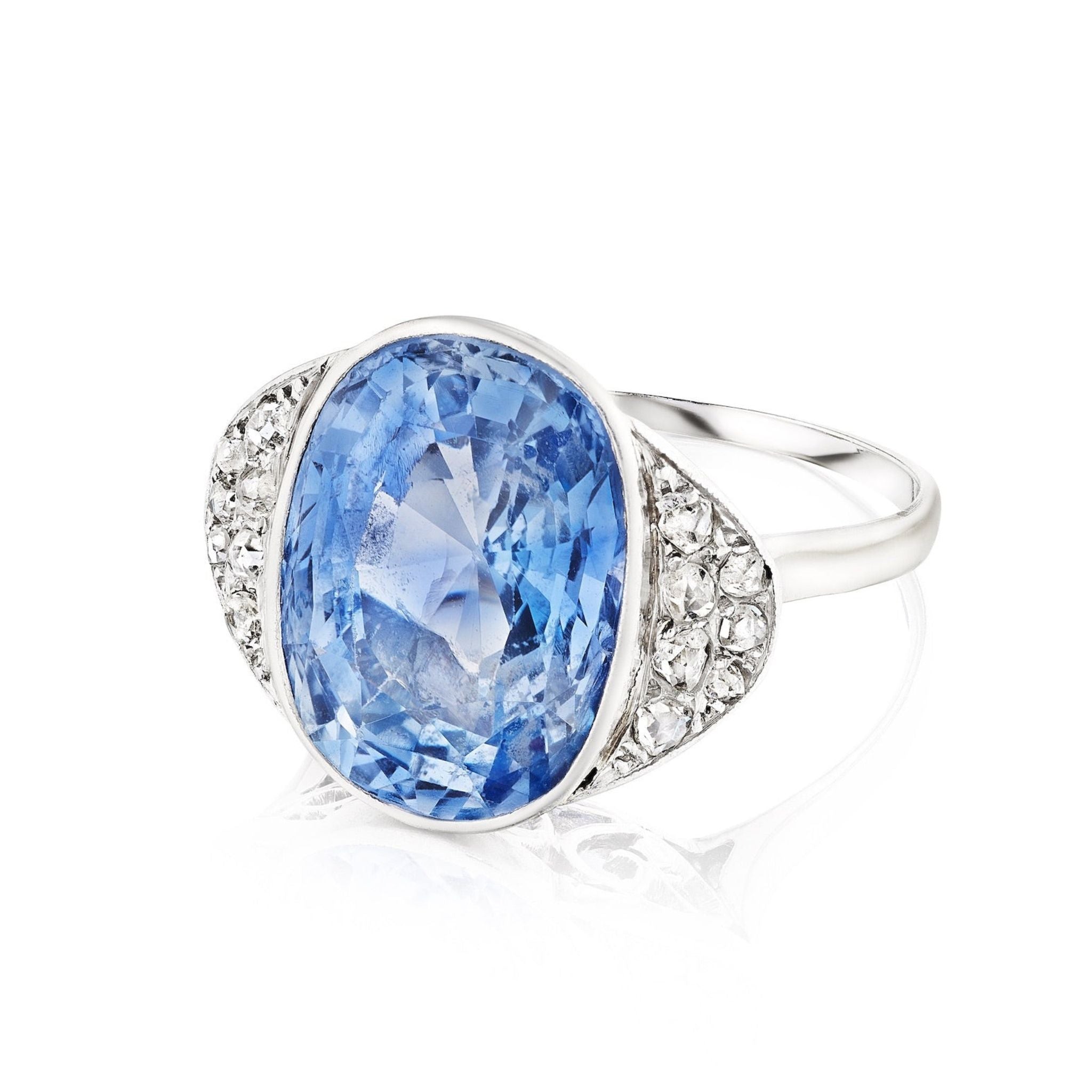 The Sapphire and Diamond Ring showcases a large oval Ceylon sapphire at its center, flanked by clusters of small rose-cut diamonds, all set in silver and displayed against a white background.