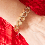 The Chrysler Hexagon Bangle with Baguette Diamonds, inspired by Art Deco style and featuring hexagonal links, is shown on a wrist above a red textured fabric background.