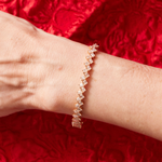 The Zig Zag Motif Emerald Cut Diamond Bangle with VS clarity diamonds is shown on a wrist, set against a textured red fabric background.