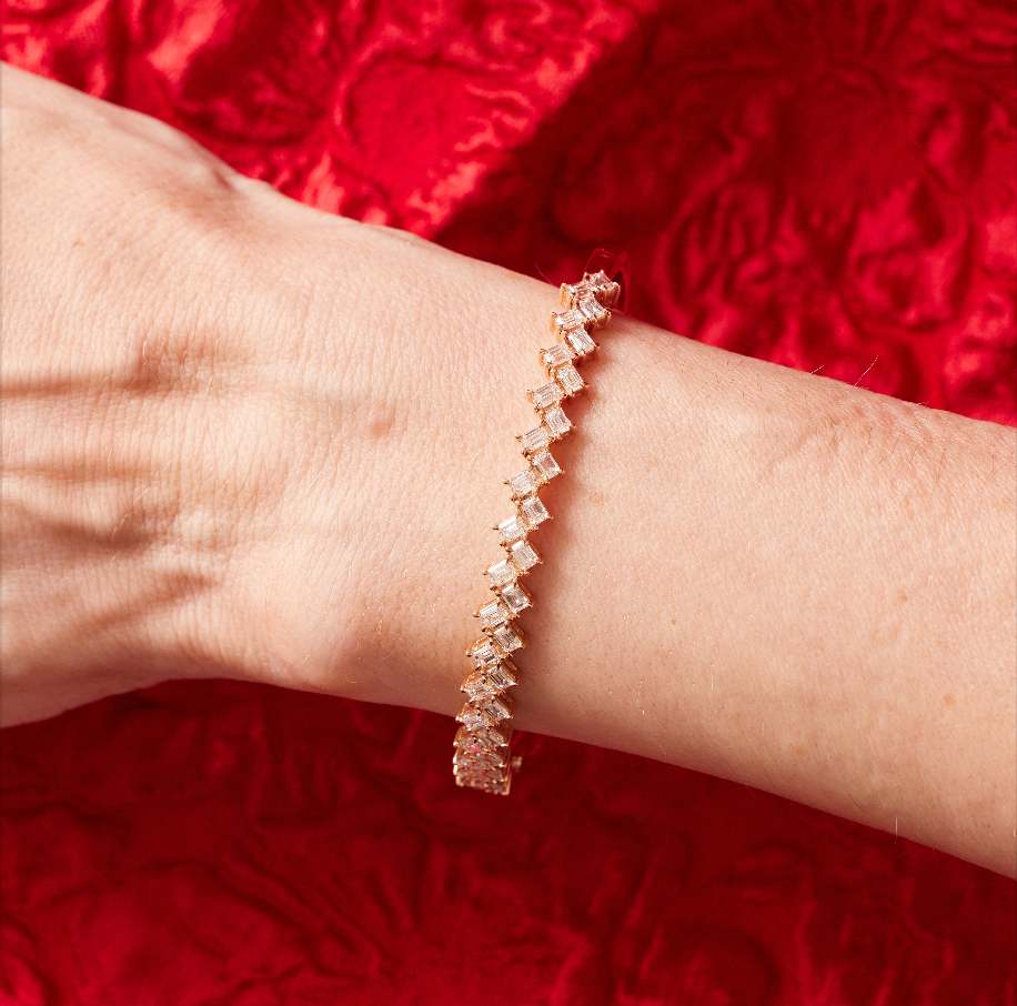 A close-up of a wrist adorned with the Zig-Zag Emerald Cut Diamond Bangle, featuring square-cut diamonds, set against red textured fabric.