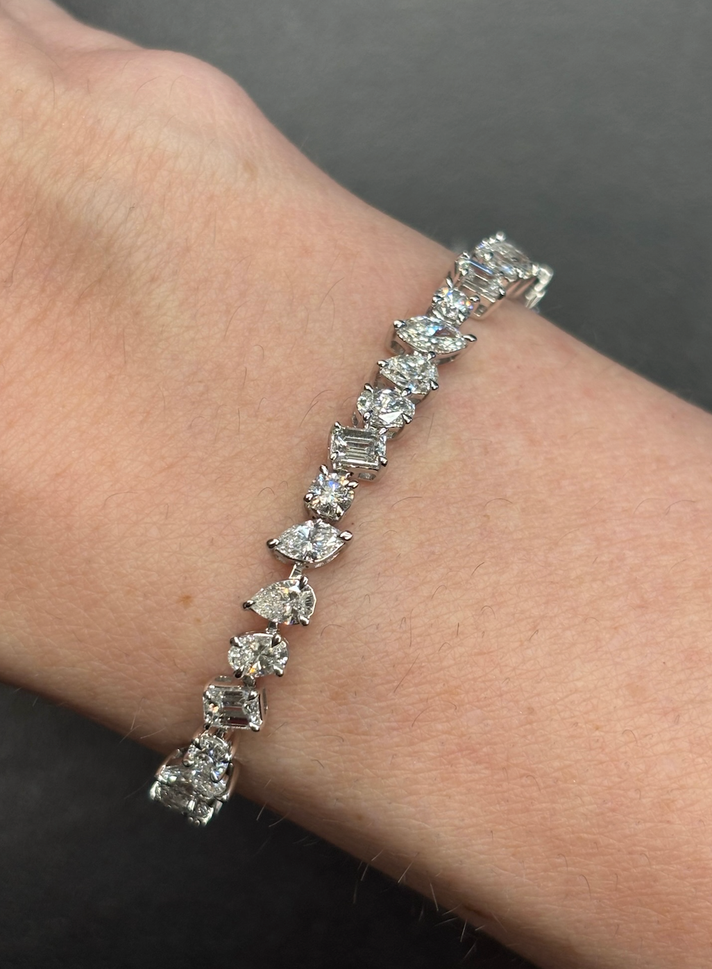 The Mixed Shape Diamond Tennis Bracelet, set with round, baguette, and marquise diamonds, sparkles on a wrist against a dark background.