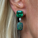 Close-up of a woman's ear wearing Asscher Cut Sapphire, Emerald, Oval Boulder Opal, and Diamond Drop Earrings in White Gold. Blonde hair partially visible; earrings feature gemstones with iridescent and sparkling details.