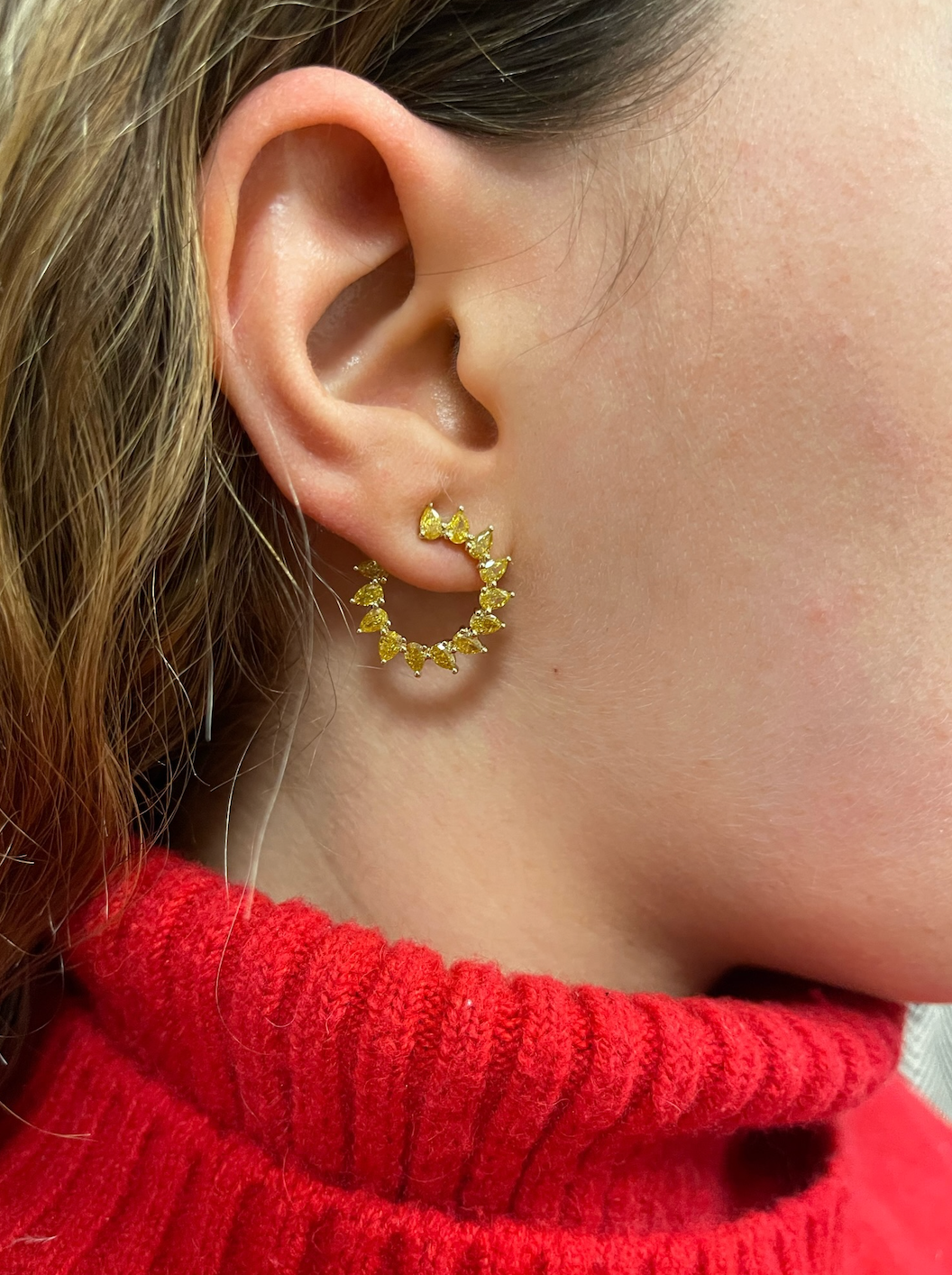 Close-up of a woman with light brown hair in a red knit turtleneck wearing Yellow Diamond Sunshine Front-to-Back Hoops, featuring gold circular design and small triangular accents in 18k yellow gold.