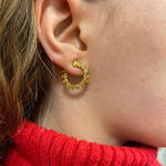 Close-up of a woman with light brown hair in a red knit turtleneck wearing Yellow Diamond Sunshine Front-to-Back Hoops, featuring gold circular design and small triangular accents in 18k yellow gold.