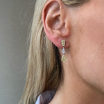 Close-up of a woman's ear wearing This & That Champagne Flute Drop Earrings with fancy yellow and white mixed shape diamonds, set in 18K yellow gold. She has blonde hair and wears a white collared shirt.