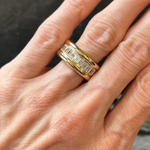 A close-up of a hand wearing two rings on the ring finger: one is plain 18K yellow gold, and the other is the Channel Set Emerald Cut Diamond Eternity Band featuring a row of rectangular emerald cut diamonds set horizontally.