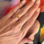 A hand with pale pink manicured nails showcases the Mixed Shape Eternity Band in Yellow Gold with Yellow Diamonds, set against a vibrant, multicolored fabric background.