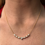 A close-up of the Mixed Shape Diamond Pendant Necklace, crafted in 18K gold, showcases seven clear diamonds—including a Heart Shape Diamond—set along its delicate chain and worn gracefully around the neck.