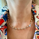 A close-up of a woman's neck wearing the Garland Chain Necklace in Yellow Gold, featuring an east-west set pear diamond. She pairs it with a vibrant blouse adorned with floral and abstract patterns.