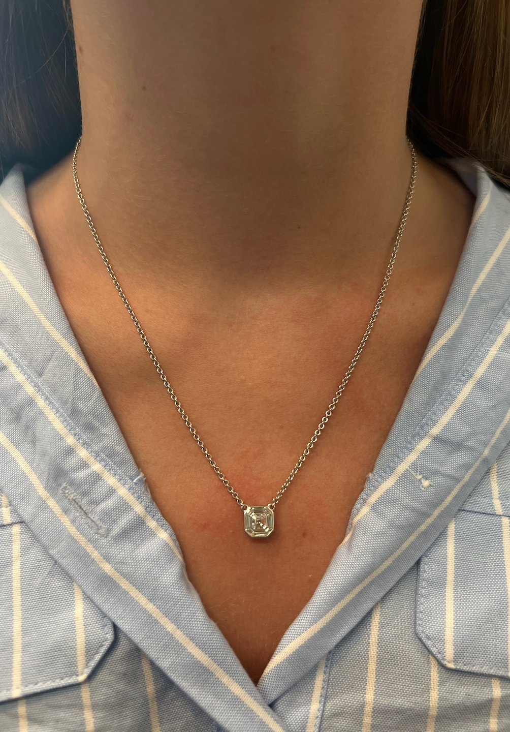 A close-up of a person wearing the Asscher Cut Diamond Mosaic Necklace in white gold, featuring a geometric pendant, shown against a blue and white striped collared shirt.