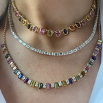 A close-up of a person’s neck wearing three layered necklaces: a gemstone choker, a bezel set tennis necklace, and the Gumdrop Necklace in Yellow Gold with Oval Multicolor Sapphires.