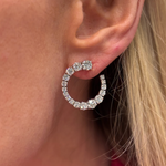 A close-up of a person’s ear adorned with the Wave Round Diamond Front to Back Hoop, crafted in 18k white gold and set with sparkling G-H color round diamonds. The wearer has straight blonde hair.
