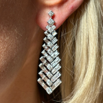 Close-up of a woman's ear wearing Art Deco Statement Earrings with round and baguette diamonds in white gold, featuring a tapering geometric pattern and sparkling details that complement her blonde hair.