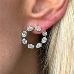 A close-up of a woman’s ear wearing Oval Diamond Front to Back Hoop Earrings in white gold. The sparkling hoops shine with diamonds, beautifully complementing her straight, blonde hair tucked behind her ear.