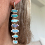 Close-up of a woman's ear wearing Opal Drop Earrings with Pavé in Yellow Gold—six oval opals set in 18K yellow gold and outlined with diamond pavé—shown against a blurred indoor background.