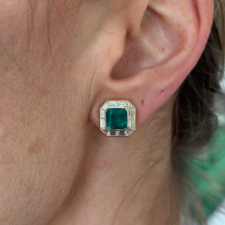 Close-up of a light-skinned person with blonde hair wearing the Mosaic Studs in Yellow Gold, featuring Asscher Cut Emeralds and baguette diamonds in a geometric setting.
