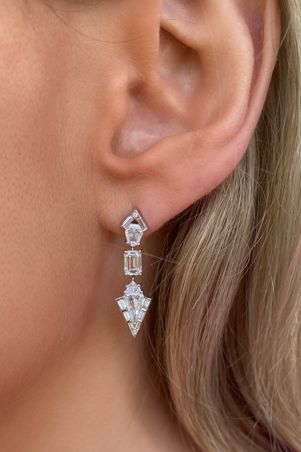 Close-up of a woman's ear wearing Statement Emerald, Baguette, and Round Cut Diamond Drop Earrings in White Gold for a modern, elegant look.