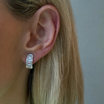 Close-up of a left ear with short blonde hair wearing the J Hoop Earring in white gold, featuring bracket bezel set emerald cut diamonds. The person wears a light green top; the earring's design echoes an emerald cut diamond style.
