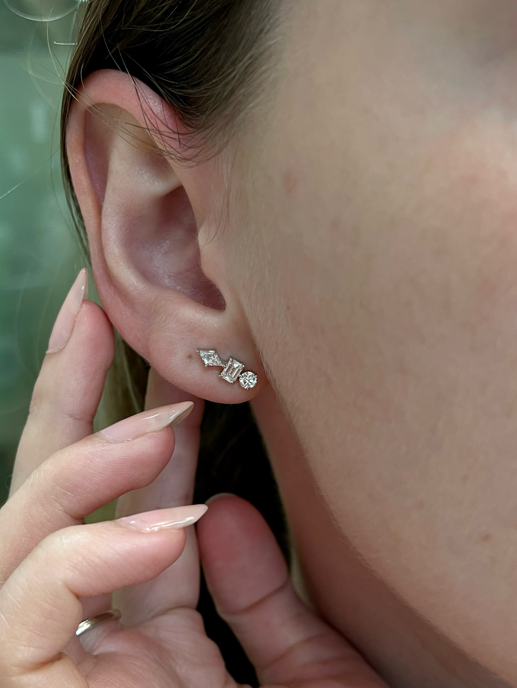Close-up of a person’s ear adorned with Straight Ear Crawlers in White Gold with Mixed Shape Diamonds. A manicured hand gently touches the earlobe, highlighting the elegant sparkle of the earrings.