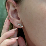 Close-up of a person’s ear adorned with Straight Ear Crawlers in White Gold with Mixed Shape Diamonds. A manicured hand gently touches the earlobe, highlighting the elegant sparkle of the earrings.